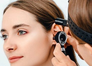 A doctor examines a woman ear with an otoscope.