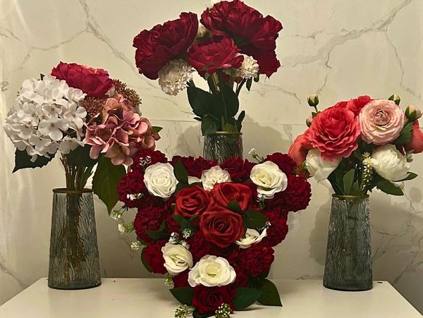 Elegant floral arrangements with red, white, and pink flowers in vases on a white surface.