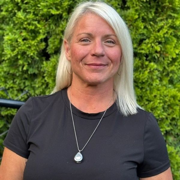 Smiling woman with blonde hair and necklace outdoors.