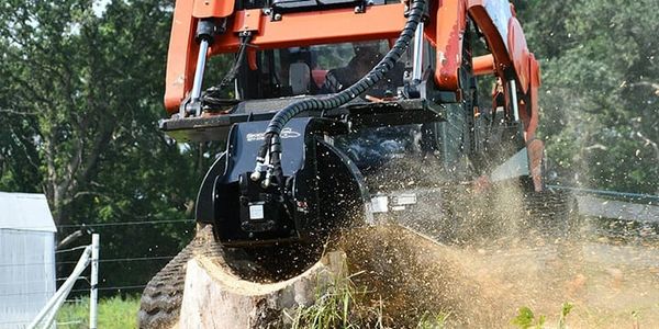 A wood chipper attached to a tractor shredding a tree stump.
