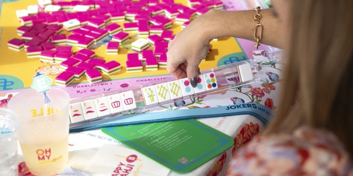 Person holding Mahjong tiles during a game on a colorful table.