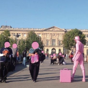 People walking near a historic building, with one person dressed entirely in pink.
