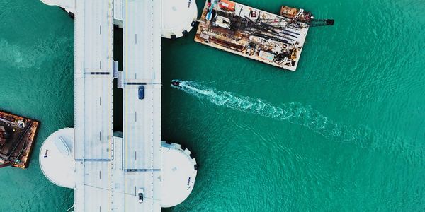 Aerial view of a bridge, turquoise water, and a boat leaving a wake.