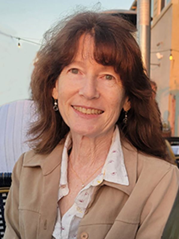 Smiling woman with brown hair in a beige jacket outdoors.