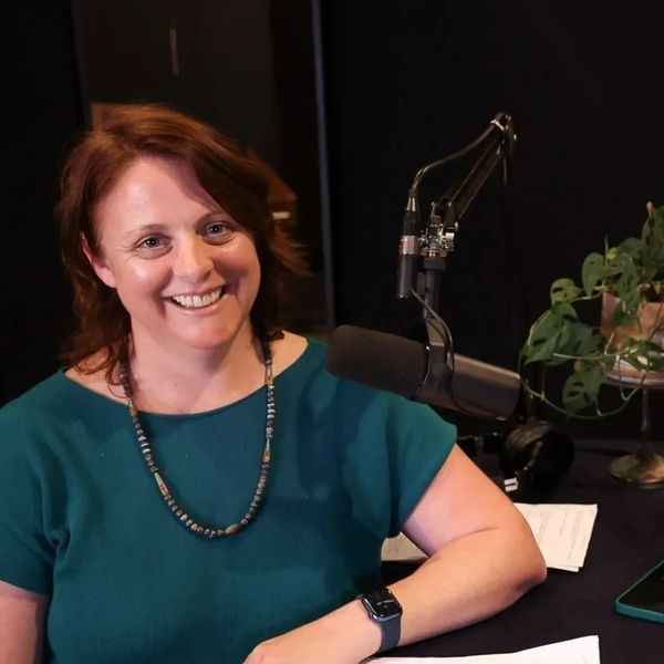 Woman smiling, with a microphone wearing a teal top.