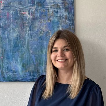 Frau lächelt vor abstraktem Gemälde an der Wand.