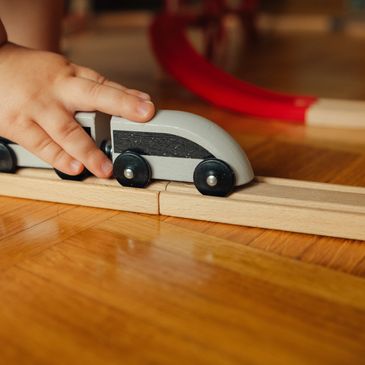 A close-up of a child's hand guiding a toy train along a wooden track.