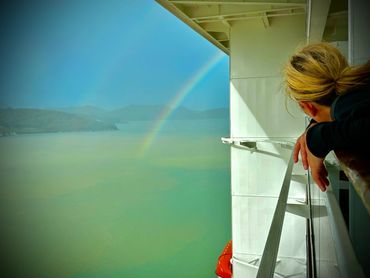 Person looks at a faint rainbow over calm water from a ship's deck.