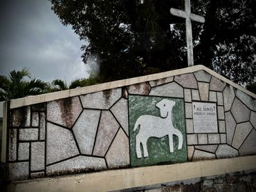 Stone wall with a lamb relief and a white cross above.