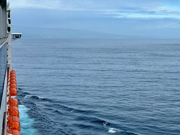 View of the ocean from the side of a ship with calm waters and a distant shoreline.
