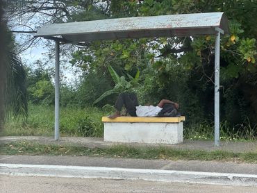A person lying down on a bench at a bus stop with a metal roof.