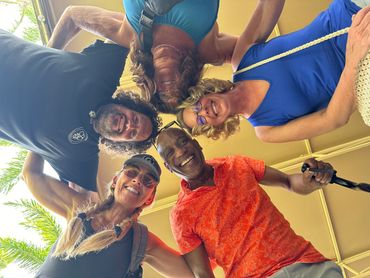 Five friends smiling in a circle, looking down at the camera outdoors.