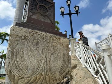 Stone carving on a pedestal with a man walking on stairs in the background.