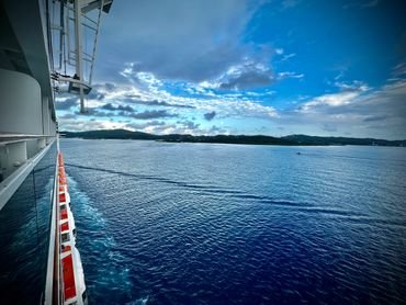 View from a ship deck showing clear blue sea and sky with distant land.