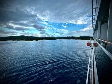 View of calm sea and distant hills from a ship deck under a partly cloudy sky.