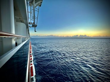 Ocean view from a ship deck during sunset with calm waters.