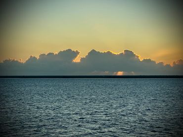 Sunset over the ocean with clouds and calm water.