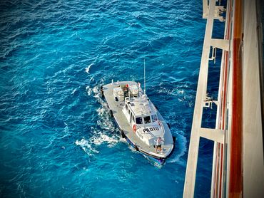 A pilot boat sails near a larger ship in deep blue ocean waters.