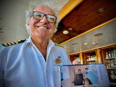 Smiling captain holding a phone showing a photo of two people aboard a ship.