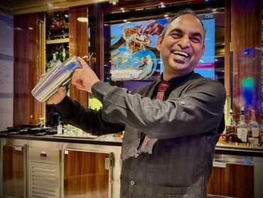 A cheerful bartender shaking a cocktail shaker behind the bar.