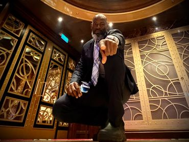 Man in suit pointing directly at the camera in a stylish indoor setting.