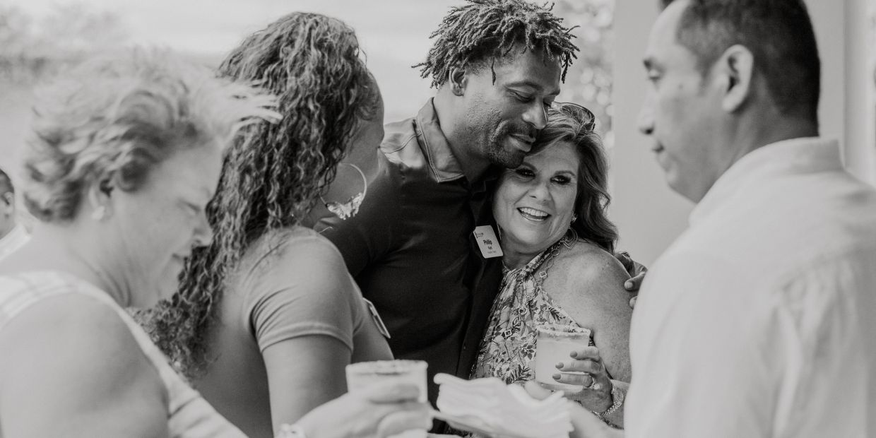 A joyful group of people sharing a warm embrace and drinks at a social gathering.
