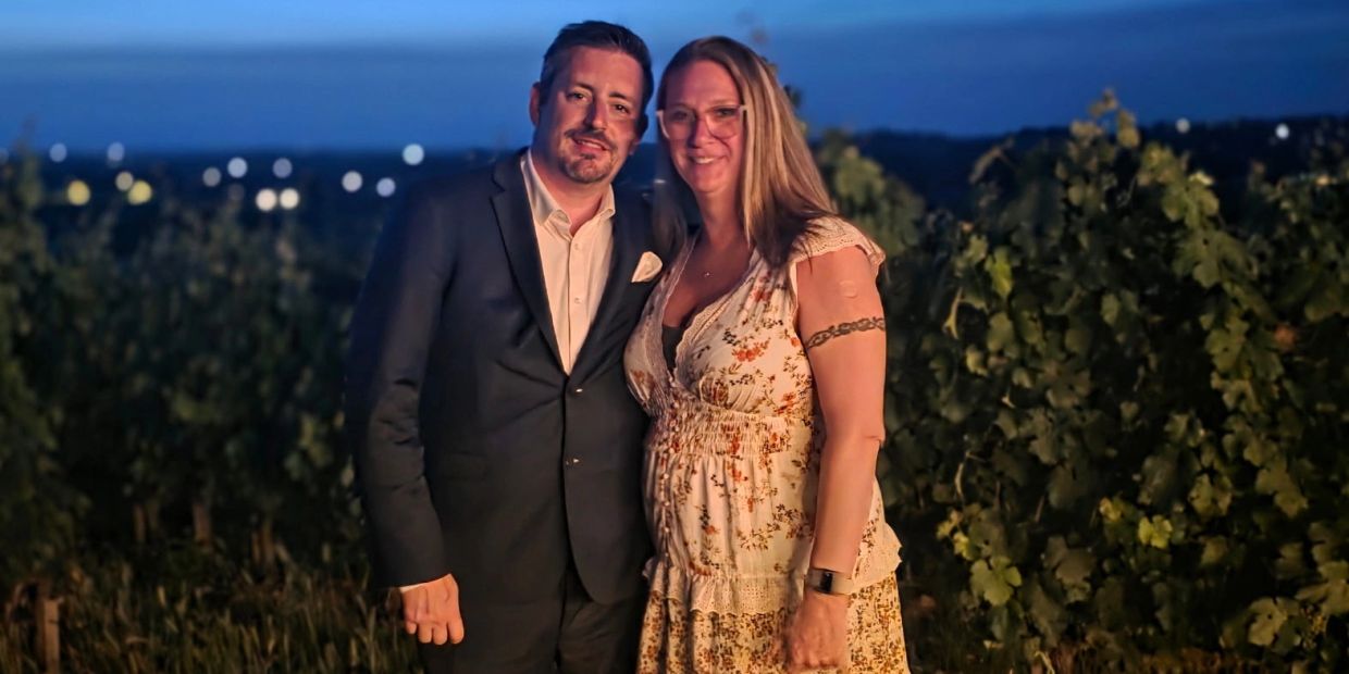 A couple posing together outdoors at dusk near greenery.