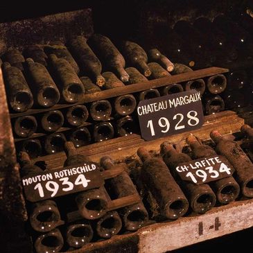 Vintage wine bottles from 1928 and 1934 covered in dust on wooden racks.