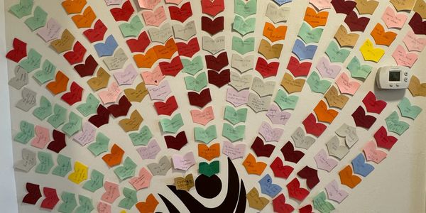 Colorful paper hearts on wall form a tree shape, each with handwritten notes.