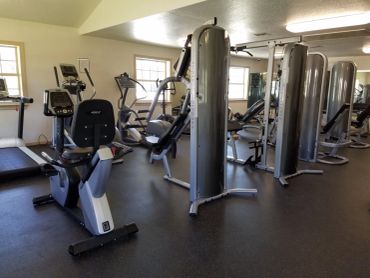 A bright gym room with various exercise machines and equipment.