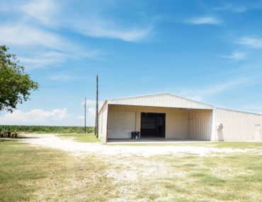A large white metal barn under a blue sky in a rural setting.