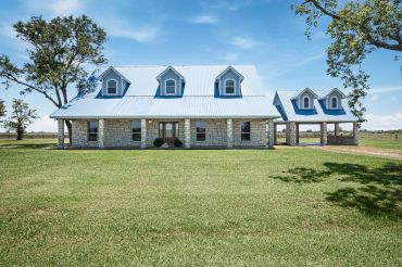 A large stone house with a metal roof and dormer windows on a sunny day.