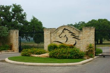 Entrance gate with horse silhouette on stone wall and greenery.