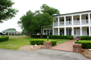 A white two-story house with green bushes and a brick walkway.