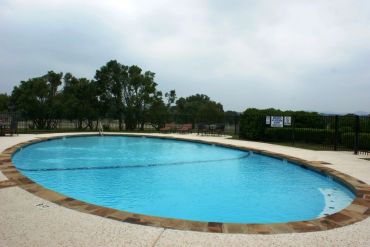 Empty outdoor swimming pool with clear blue water under a cloudy sky.