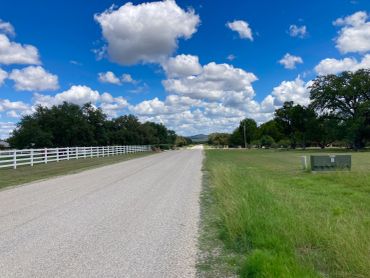 A rural road under a blue sky with fluffy clouds and green grass.