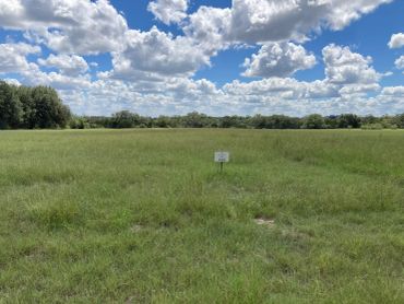 Open grassy field under a partly cloudy sky with a small sign in the center.