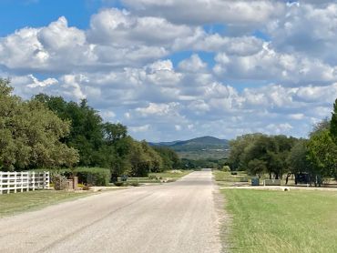 A peaceful rural road with trees and hills under a partly cloudy sky.