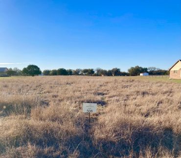 Empty lot with dry grass and a sign reading '506' under a clear blue sky.