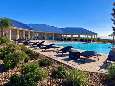 Sunny outdoor pool area with lounge chairs and blue-roofed buildings.