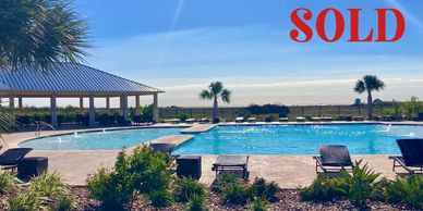 A sunny poolside with lounge chairs and a 'SOLD' sign in red.
