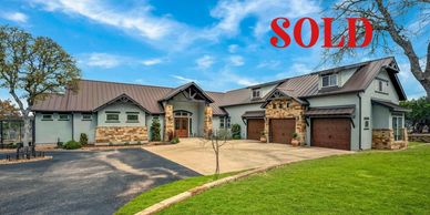 Modern large house with stone accents and sold sign on front.