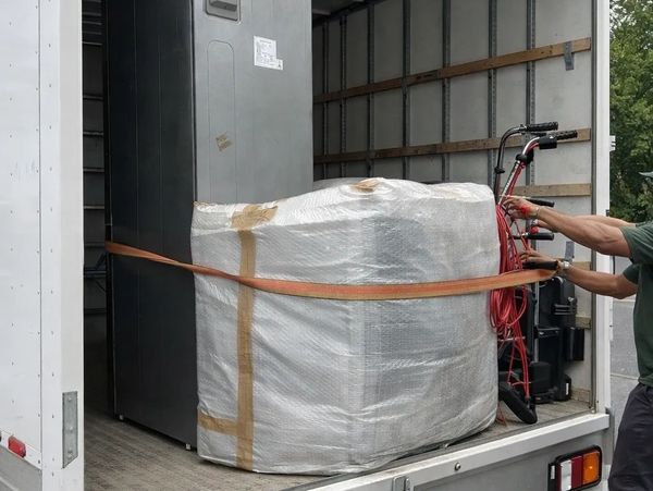 Large appliance secured inside a moving truck with straps and plastic wrap.