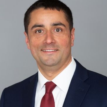 Professional headshot of a man in a suit and red tie.