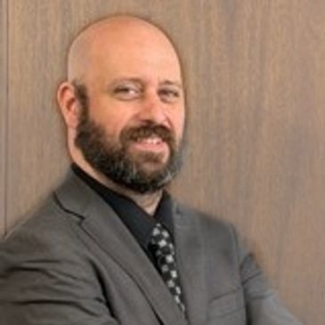 Smiling bald man with beard in suit.