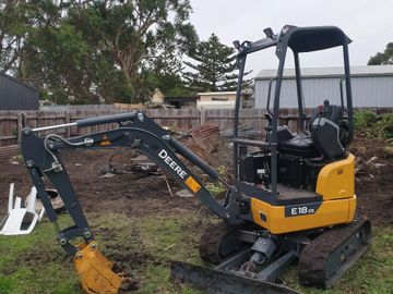 A Deere E18 ZS mini excavator parked on grass with a dirt patch in a backyard.