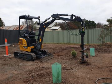 A small excavator with an auger attachment digging holes in a backyard.