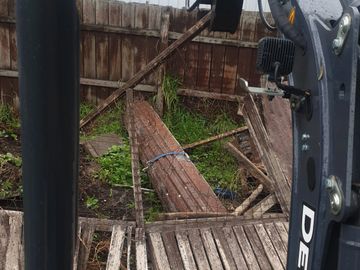 Broken wooden fence panels lying on the ground near a Deere machine.