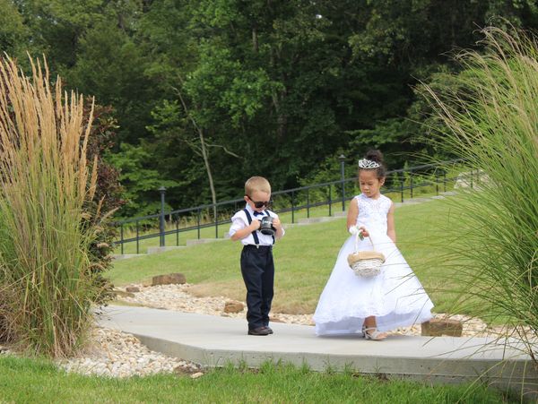 Two children dressed formally, a boy with sunglasses and a girl in a white dress holding a basket.