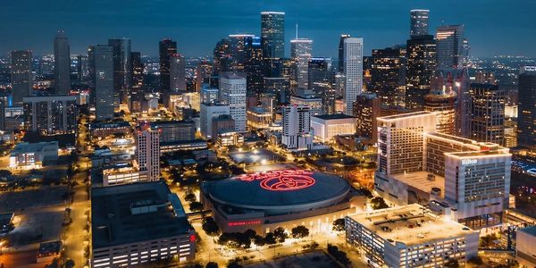 A vibrant city skyline at dusk with illuminated buildings and a large arena.